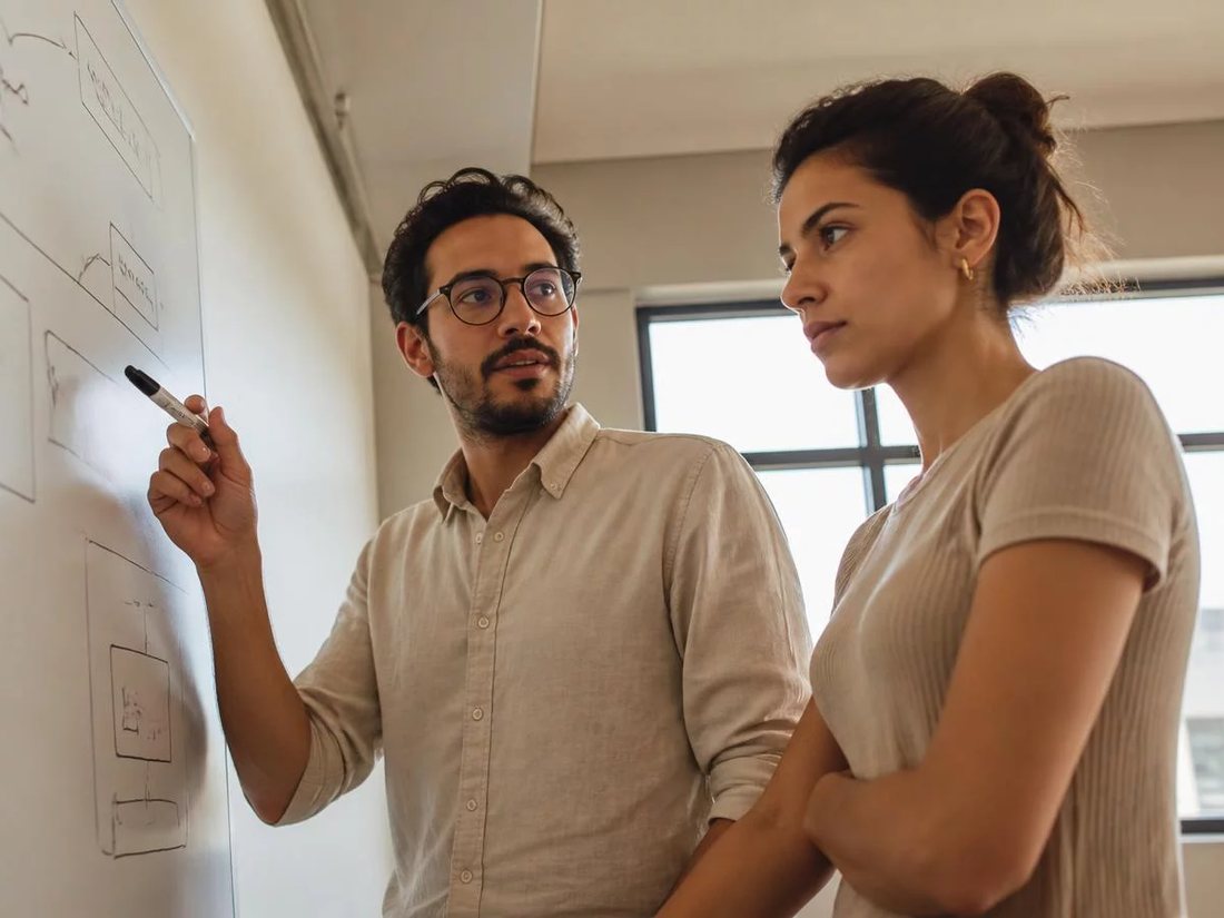 Duas pessoas diante do quadro branco com a armação de um argumento rabiscada